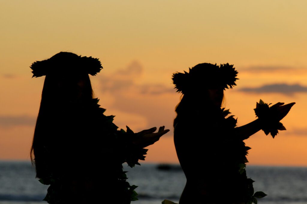 Image of two woman dancing hula at evening luau.
