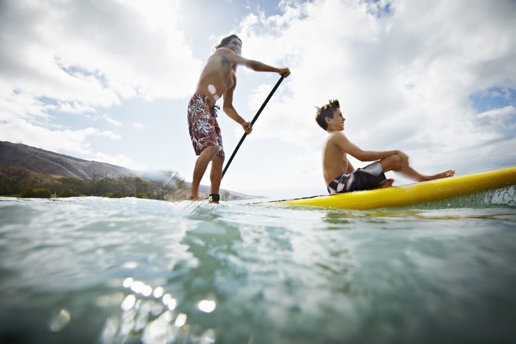 Father and son stand up paddleboarding with son sitting