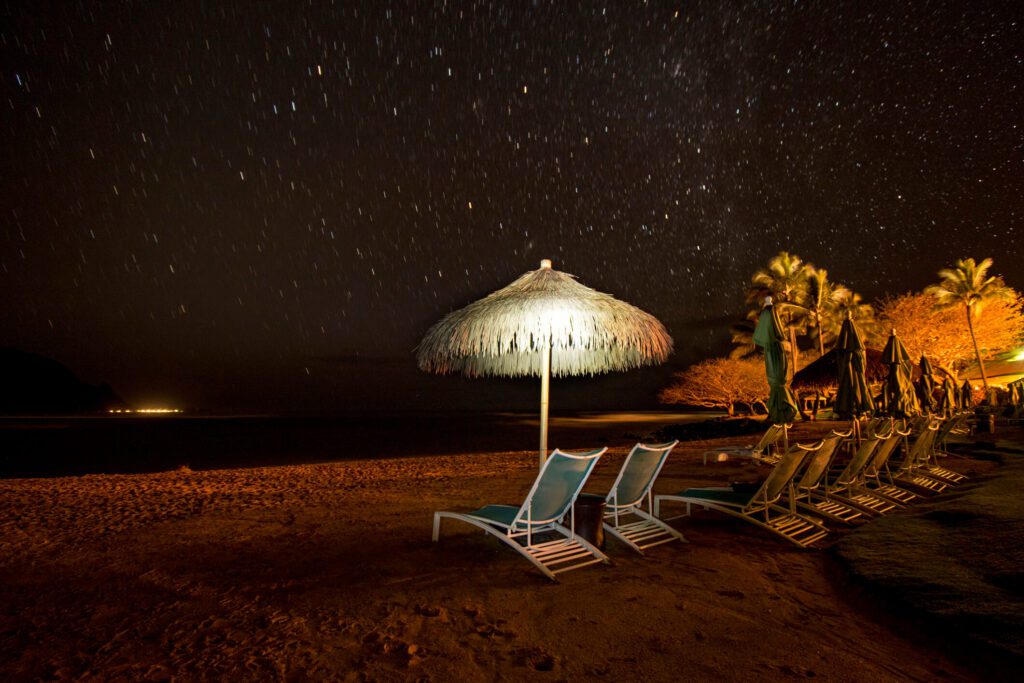 The beach at night in Maui, Hawaii with several beach chairs and umbrellas.
