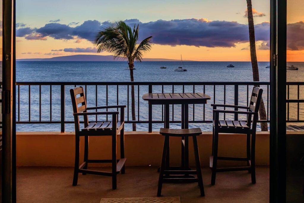 Two chairs and a table on an oceanfront balcony view at sunset on Maui.