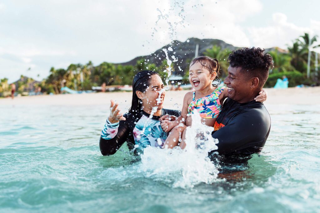 Young girl laughing while splashing in the ocean with her aunt and uncle