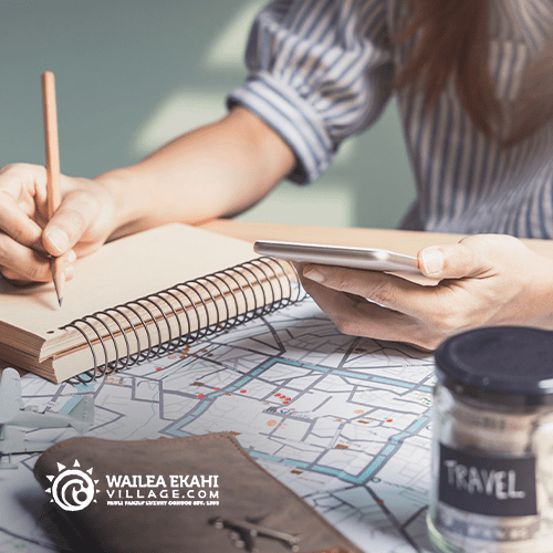 Picture of a woman writing in a notebook and looking at her phone to plan a vacation