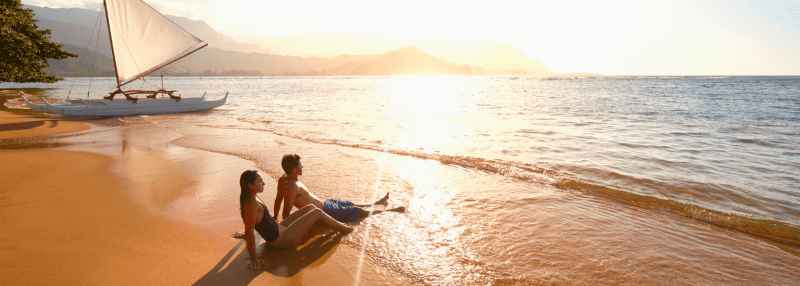 Couple sitting on the beach in Hawaii looking out at the ocean
