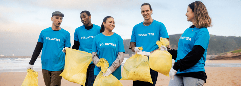 Group of people dressed in blue shirts with volunteer on them, carrying yellow sacks during beach cleanup
